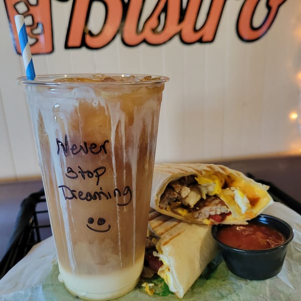 Iced coffee with "Never Stop Dreaming" and a breakfast burrito with salsa at Uplifted Bistro.