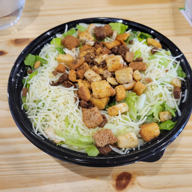 Uplifted Bistro's Caesar salad with shredded cheese and croutons in a black bowl on a wooden table.