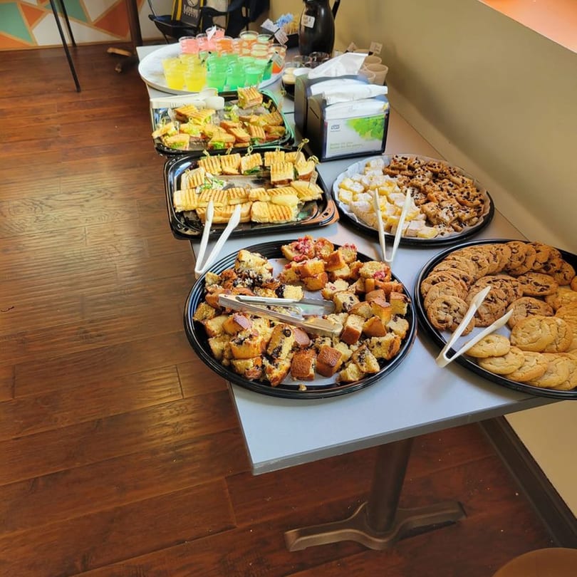 A table laden with Uplifted Bistro's cafe food, including mini sandwiches, pastries, and cookies.