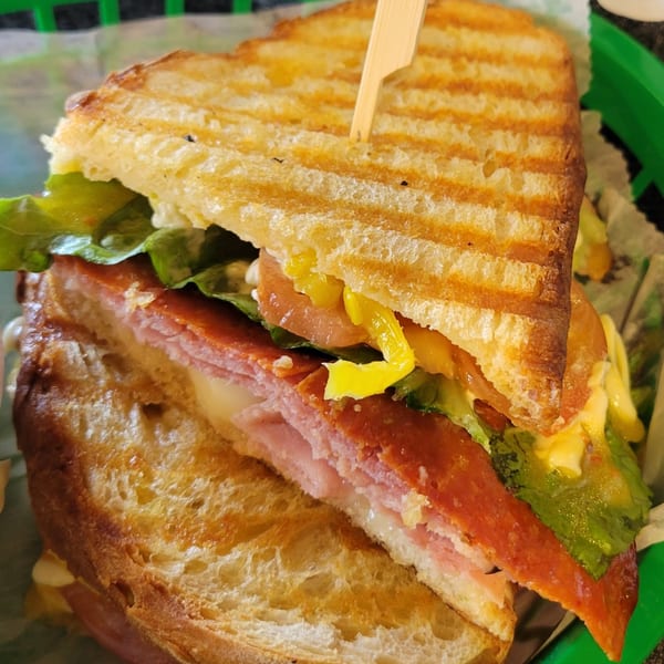 A grilled Uplifted Bistro sandwich with ham, pepperoni, cheese, lettuce, tomato, and peppers.