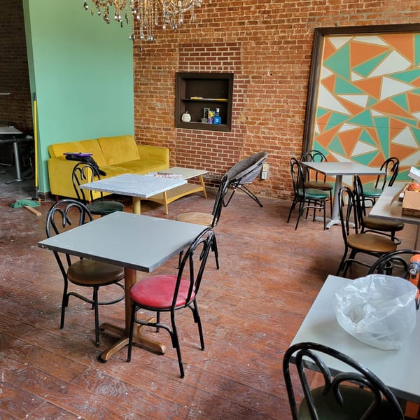 Uplifted Bistro's cafe interior with brick walls, a yellow sofa, and scattered tables and chairs.