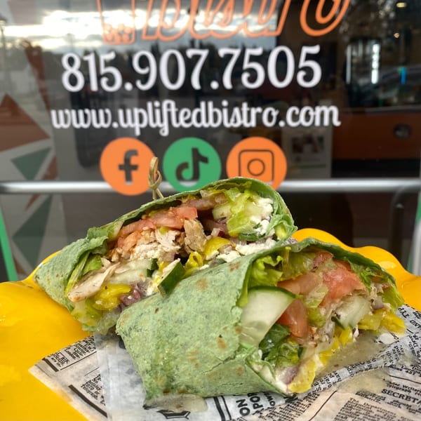 A vibrant green wrap, filled with fresh vegetables and chicken, sits on newspaper-lined paper.