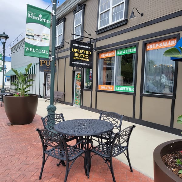 Uplifted Bistro's storefront with outdoor seating, displaying menu items like boba, sandwiches, and coffee.