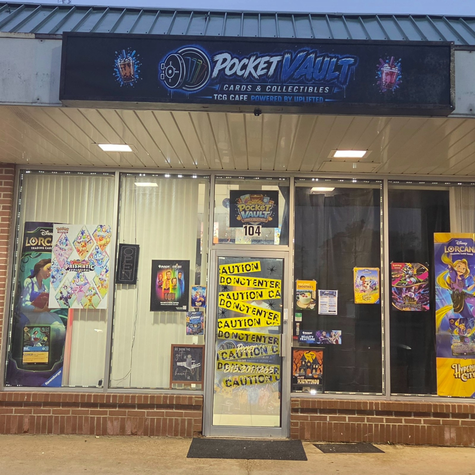 Exterior storefront of Pocket Vault TCG Cafe displaying trading card game posters, collectibles, and caution signs in the windows.