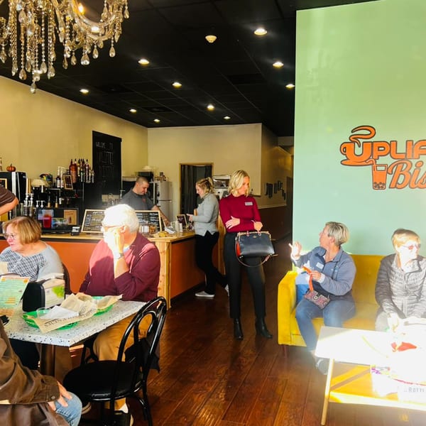 Customers seated at tables and on a yellow couch inside Uplifted Bistro, with staff behind the counter.