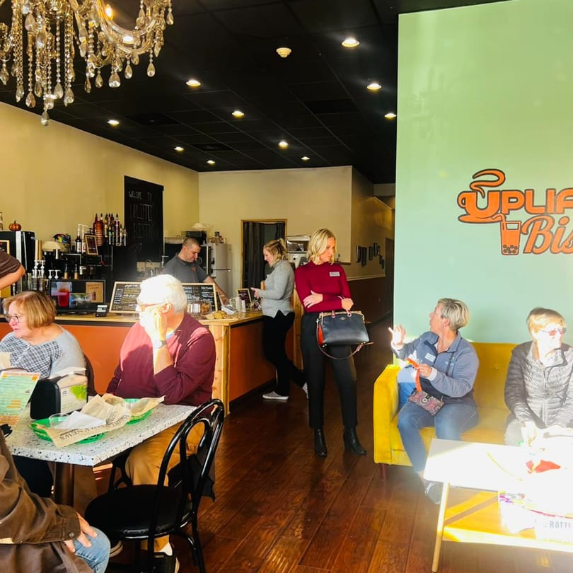 Customers seated at tables and on a yellow couch inside Uplifted Bistro, with staff behind the counter.