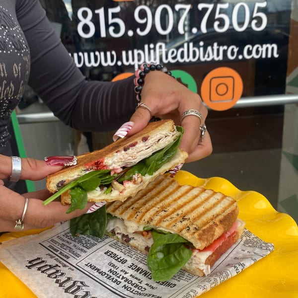 Hands hold a turkey and cranberry panini, with another on a yellow plate, from Uplifted Bistro.