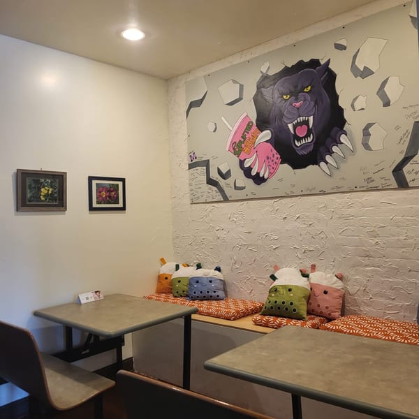 Uplifted Bistro's cafe interior with a large panther mural, tables, and boba tea plush pillows.