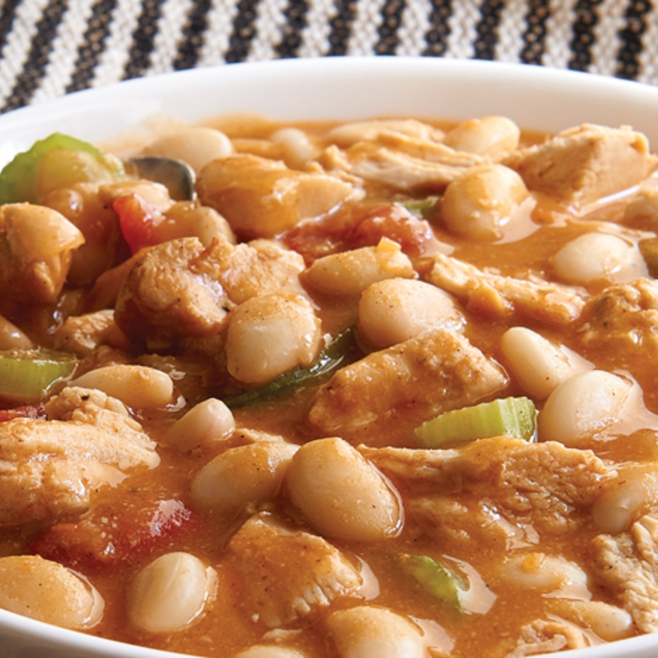 Close-up of chicken and white beans simmered with vegetables in a rich brown sauce, served in a white bowl.