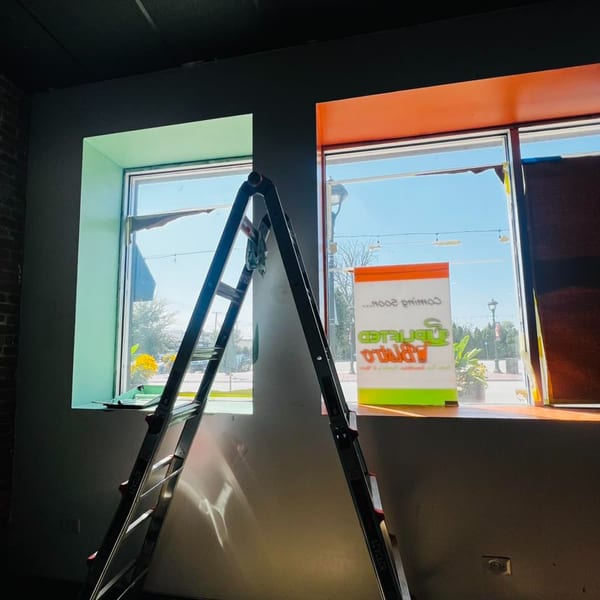 Interior view of Uplifted Bistro with a ladder, colorful window frames, and a "Coming Soon" sign.