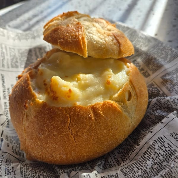 A bread bowl filled with creamy mac and cheese, served on newspaper at Uplifted Bistro.