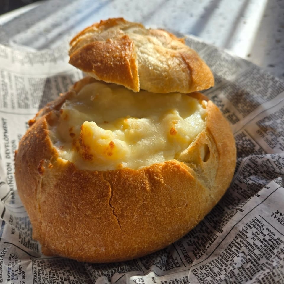 A bread bowl filled with creamy mac and cheese, served on newspaper at Uplifted Bistro.