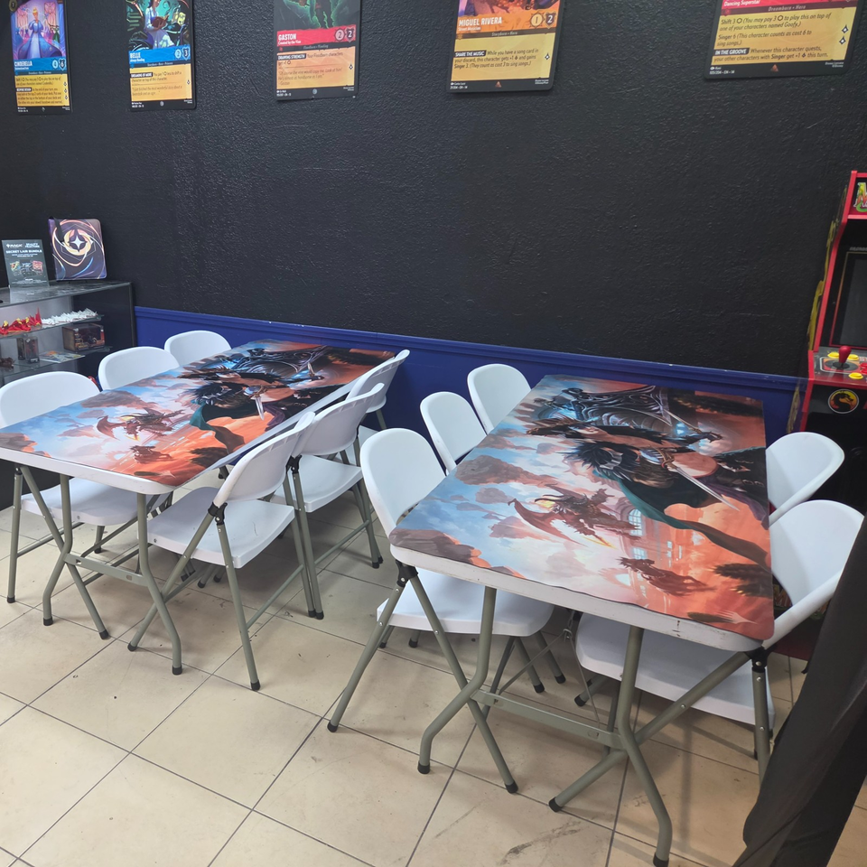 Game-themed venue with colorful character cards on the wall, illustrated tables, white folding chairs, and an arcade cabinet.