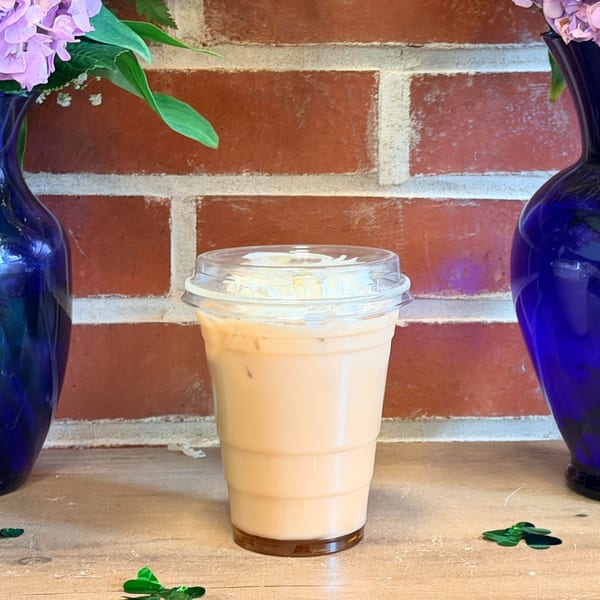 Iced latte in a plastic cup with a brick wall background and blue vases with flowers.