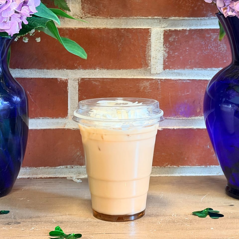 Iced latte in a plastic cup with a brick wall background and blue vases with flowers.