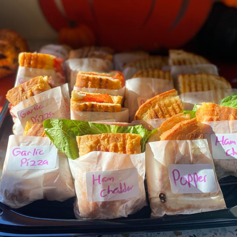 Assorted Uplifted Bistro cafe sandwiches, including "Garlic Pizza," "Ham Cheddar," and "Popper" varieties, wrapped in paper.