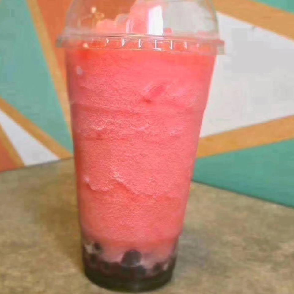 Red blended fruit drink with dark tapioca pearls in a clear plastic cup on a colorful table.