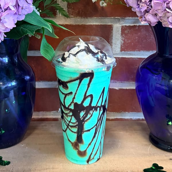 Mint green Uplifted Bistro drink with whipped cream and chocolate drizzle, flanked by blue vases with flowers.